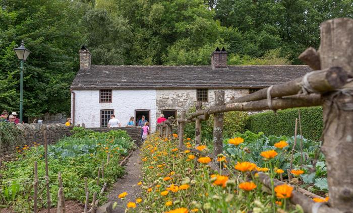 image shows a short row of 3 small cottages. they have grey tiled rooves and brick chimneys. in the foreground, you can see the cottage garden, plante